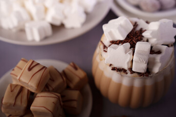 cozy dessert scene with hot beverage topped by star-shaped marshmallows and chocolate sprinkles, accompanied by plates of white fluffy confections and neatly arranged caramel-draped treats, decadent