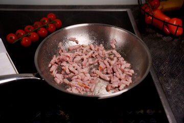 cooking scene with bacon pieces sizzling in a pan on a modern stovetop, adorned with vibrant red cherry tomatoes and a basket of colorful vegetables, evoking a fresh culinary atmosphere, homemade
