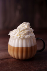 creamy latte in a textured glass mug on wooden surface with rich whipped cream top against a dark, cozy backdrop, evoking warmth and comfort, focus, blurred, moist, pleasure, stylish, calming, sweet