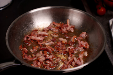 sizzling bacon cooking in a stainless steel pan with golden crispy texture and juices against dark kitchen background, preparation, roast, tempting, seasoned, savory, homemade, simmering, breakfast