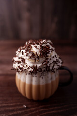 close-up of a creamy coffee topped with whipped cream and chocolate sprinkles in a decorative glass mug against a dark wooden background with warm, cozy ambiance, flavorful, culinary, luxurious