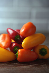 a vibrant assortment of mini bell peppers in red, orange, and yellow hues, stacked artfully against a soft-focus tiled background, exuding freshness and culinary potential, simplicity, reflection