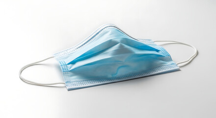 A light blue surgical mask with white elastic ear loops on a white surface in a studio setting ai generated