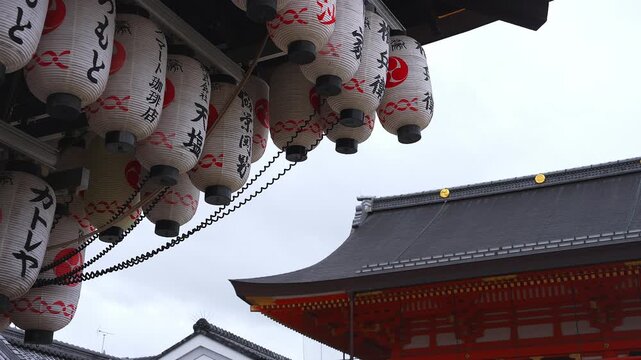 Dozens of white lanterns with black kanji and red emblems sway beside a vermilion temple gate at Senso ji in Asakusa, Tokyo, shot daylight under overcast.