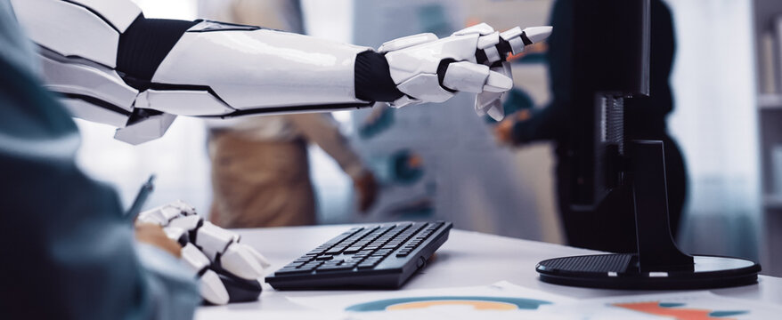 A robotic arm points at a computer screen displaying data in a contemporary office, highlighting teamwork and technology in a productive business environment.Noogenesis - Powered by Adobe