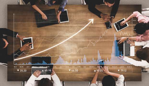 Aerial view of diverse professionals engaged in a collaborative meeting, analyzing financial data and trends using modern technology in a contemporary office setting. Scalp