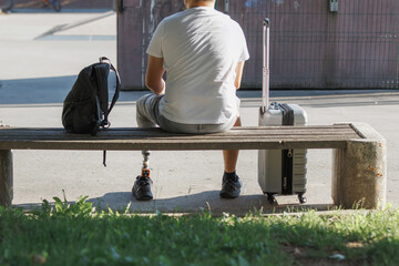 Man with a prosthetic leg on the journey, sitting on the bench using a laptop while waiting for a...