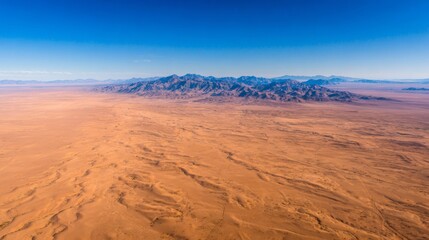 Fototapeta premium Arid desert landscape with distant mountains under a clear blue sky, showing vast empty wilderness aerial view