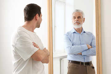 Young man seeing himself as senior in mirror. Concept of personality, past and future, flow of time, age