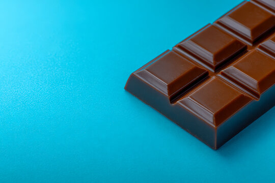 Smooth milk chocolate bar with separated segments resting on a vibrant blue surface perfect for confectionery and dessert themes