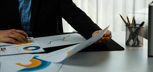 A focused businessperson examines financial reports filled with charts and graphs at an organized...
