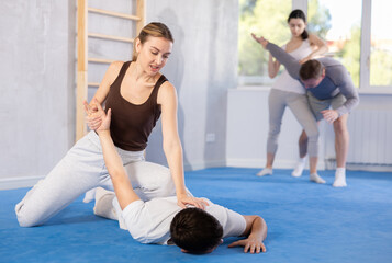 Obraz premium Irate young female trainee applying armlock technique on person in sports hall