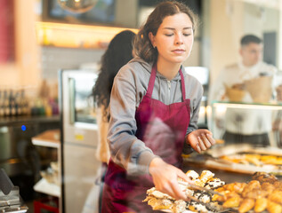 Girl canteen worker waits for customers near bakery counter, ready willing to sell fresh bun, help...