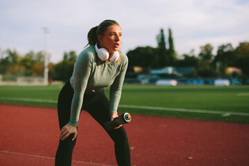 Exhausted but focused Caucasian female athlete leans on her knees to catch her breath on a running track after a strenuous and intense outdoor workout
