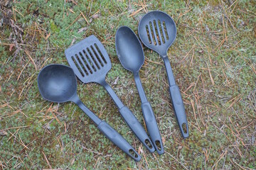 a set of four black plastic kitchen utensils lie on the ground and green moss on a summer street