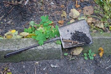 one old black iron scoop a pile of trash lies on a gray concrete curb on a summer street