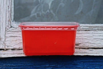 One red closed plastic box stands on a blue white table on a summer street