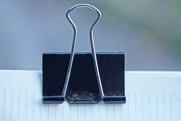 A single black metal paper clip holds together the white sheets of a notebook