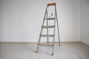 Metal stepladder with paint brush and tray in an empty room during wall renovation. Clean interior and floor ready for painting work.