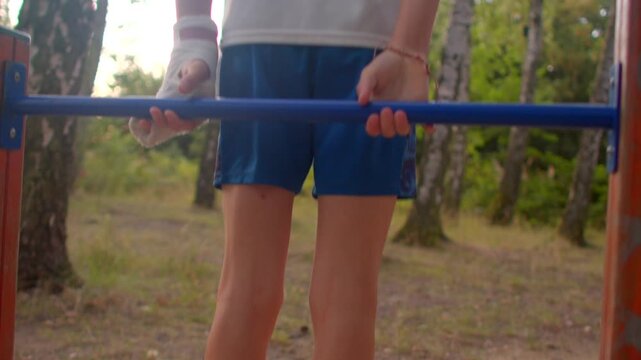 Young martial artist performing dips on outdoor fitness bars amid woodland surroundings under gentle sunlight