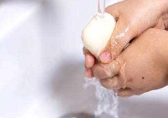 A child's hands are being washed with soap under a running tap