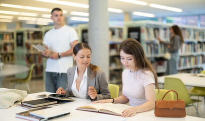 Female students study together, they work at the table, make notes in a notebook and read books. Students prepare for admission in the new academic year