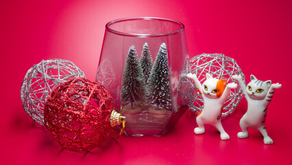 Funny dancing cat figurines and Christmas decorations on a festive red background. Whimsical and...