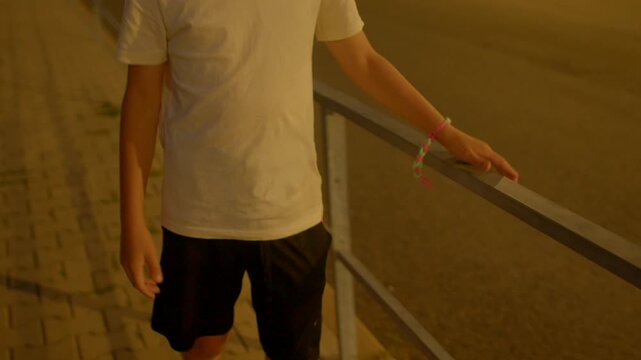 Young individual walks securely alongside rail, Casual youth maintains stability using handrail during evening
