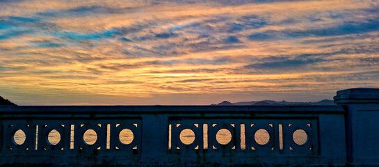 Beautiful sunset view over the ocean in Santos, São Paulo, Brazil, seen through the traditional seaside balustrade. The colorful sky and calm sea create a peaceful and scenic coastal atmosphere.