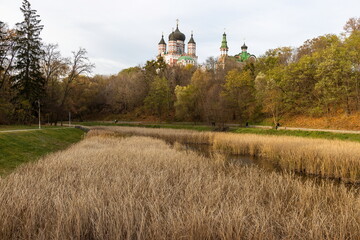 Orthodox church overlooking autumn park with dry grass and pond