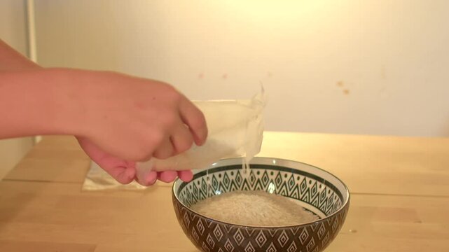 Preparing sushi with rice and utensils shown, Closeup of hand transferring rice into bowl for sushi