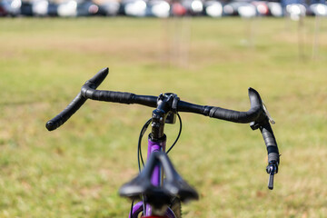 Front view of a road bike&rsquo;s handlebar and saddle, showing drop-style grips, integrated brake levers, and ergonomic cockpit design in an outdoor setting. Selective focus.