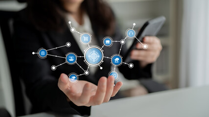 A businesswoman engages with her smartphone while surrounded by digital icons symbolizing global networks and technology in a modern office environment. Tessel
