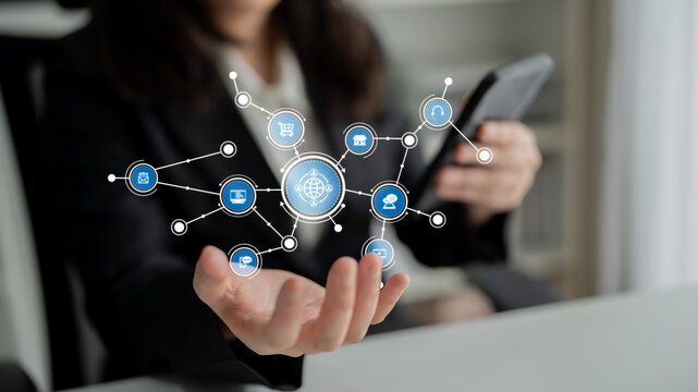 A businesswoman engages with her smartphone while surrounded by digital icons symbolizing global networks and technology in a modern office environment. Tessel