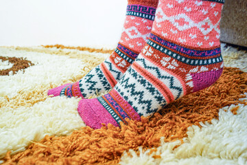 Woman wearing knitted patterned socks standing on shaggy rug. Symbolizes comfort zone, cold weather coziness, minimal lifestyle, tactile textures, self-care, seasonal atmosphere, and peaceful morning.