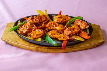 Indian cuisine Tikka chicken in a cast iron dish served hot at the table garnished with bell pepper spears