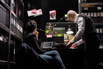 Detective officers study surveillance photos on a mystery board, using investigative tools to trace criminal activity and uncover proof. Identifying a suspect responsible for illegal operation.