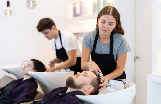 Young female hairdresser stylist washing hair of young male client in beauty salon