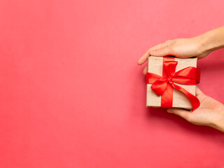 hand gift presentation, closeup of hands cradling miniature gift wrapped with care, intimate closeup image featuring hands gently holding small decorated package against vibrant red backdrop
