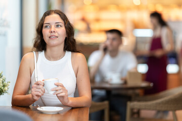 Young European woman enjoys a cup of hot quality coffee made from Arabica beans. Woman enjoys drinking cappuccino in a coffee shop