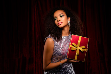 Stunning young woman holding a gift box with a gold ribbon, dressed in shimmering outfit and glamorous makeup