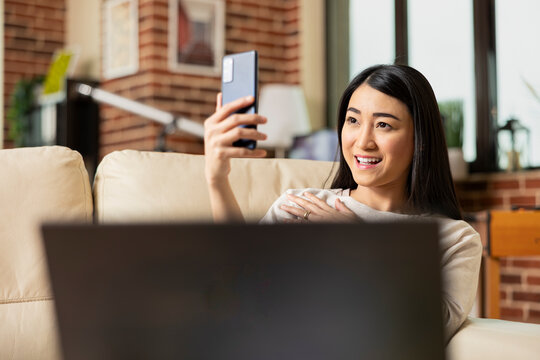 Happy businesswoman relaxes on sofa, taking selfie with smartphone. Cheerful female freelancer captures moment for social media while enjoying downtime at home with mobile device in hand.