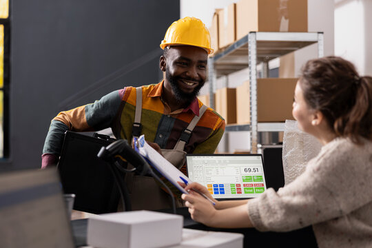 Diverse employees checking inventory list and order processing systems for express delivery operations, preparing packages for distribution. Small scale e-business activity and online shopping.