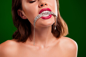Elegant woman biting a sparkling silver bracelet against a vibrant green background, showcasing beauty and glamour