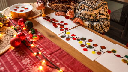 Children painting Christmas lights on paper at a festive holiday table