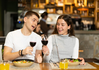 Happy couple chatting, drinking red wine and eating delicious dishes in a European restaurant. Man and a woman are sitting against the background of a cozy interior in a restaurant.