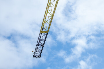 Fototapeta premium Construction crane arm reaching towards a bright blue sky with fluffy white clouds, showcasing industrial machinery and engineering in an urban environment with copy space