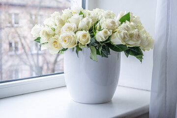 White roses arranged beautifully in a modern white vase on a windowsill, creating an elegant atmosphere perfect for celebrations and anniversaries with copy space