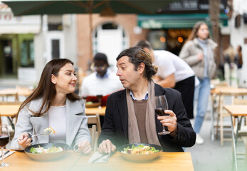 Girl in cafe sits near male companion, has nice conversation and discusses news of day. Cozy atmosphere of cafe, meeting place for friends, business partners, colleagues.