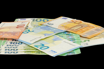 Pile of assorted euro banknotes including one hundred, fifty, twenty, ten and five euro notes scattered on a plain black background, studio shot in tilted view, close-up macrophotography.